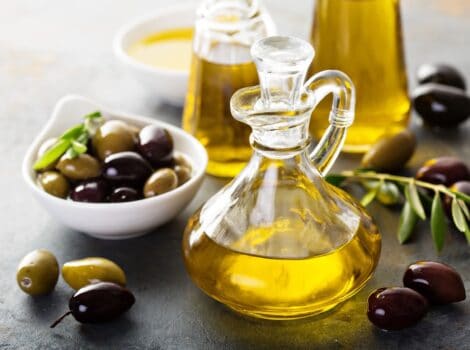 Horizontal shot of a glass bottle filled with olive oil sitting next to a white dish of green and black olives.