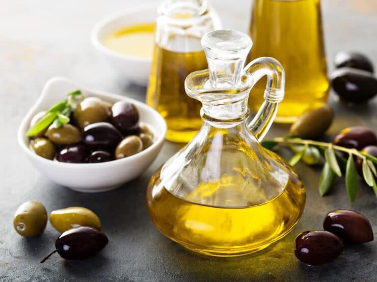 Horizontal shot of a glass bottle filled with olive oil sitting next to a white dish of green and black olives.