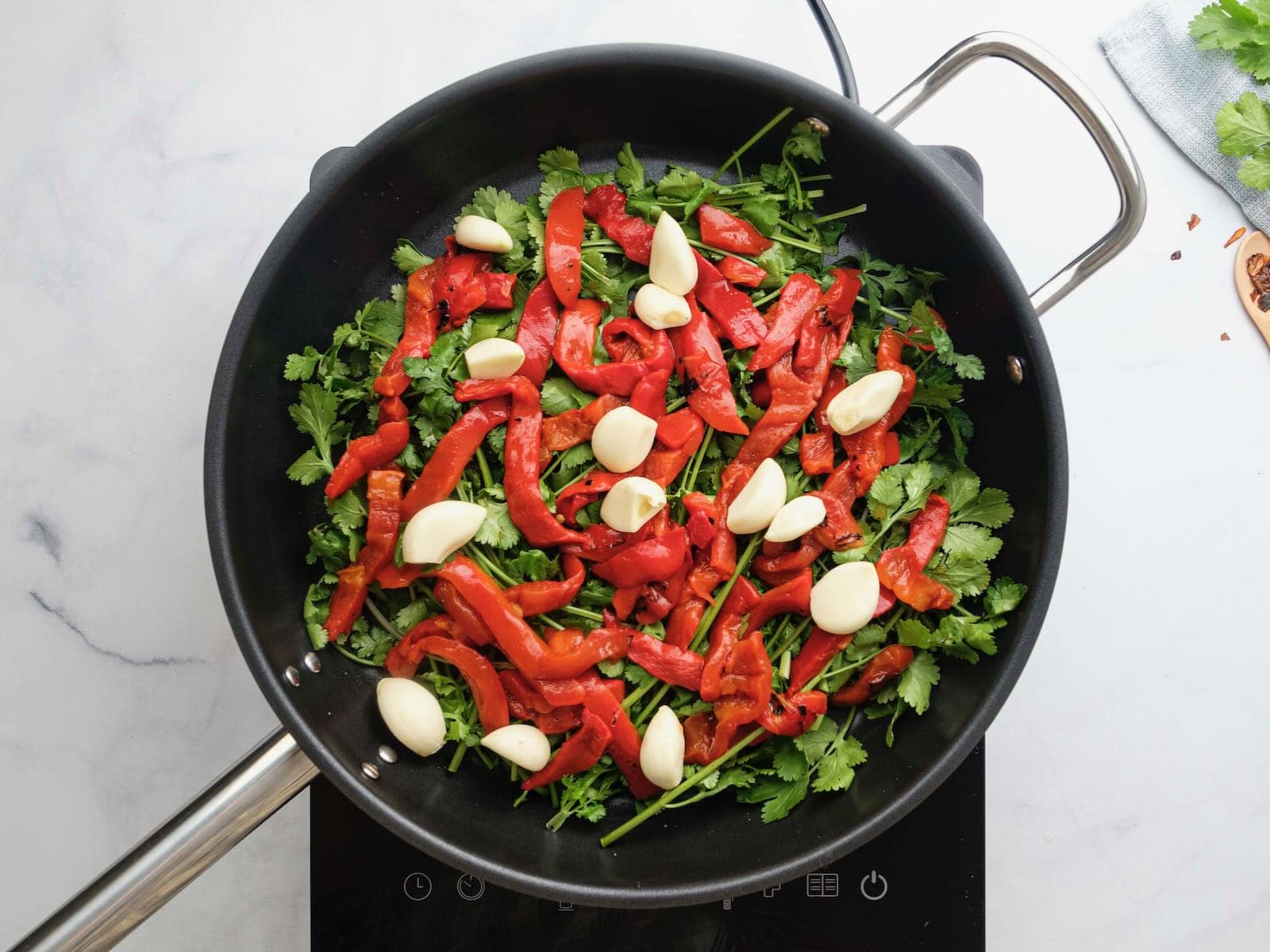 Horizontal overhead shot of a sautee pan filled with greens, red peppers, and garlic cloves.