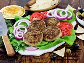 Horizontal Shot - plate with four grilled Mediterranean Turkey Burgers with onion slices, tomato slices and a bed of fresh green lettuce. Hummus, pita chips, and a dish of olives in the background.