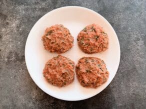 Four soft turkey burger patties loosely formed, uncooked on white plate, grey surface beneath.