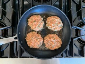 Four half-cooked turkey burger patties cooking in a nonstick skillet, sizzling with olive oil on stovetop.