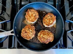 Four turkey burger patties cooking in a nonstick skillet, sizzling with olive oil on stovetop.