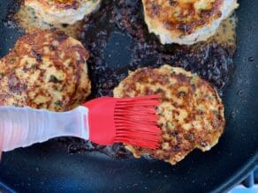 Close up - silicone brush brushing turkey burger patty with olive oil in nonstick skillet.
