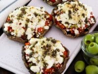 Featured square shot - Four beautiful stuffed portobello caps with goat cheese on a platter, with green olives and a linen towel beside them.