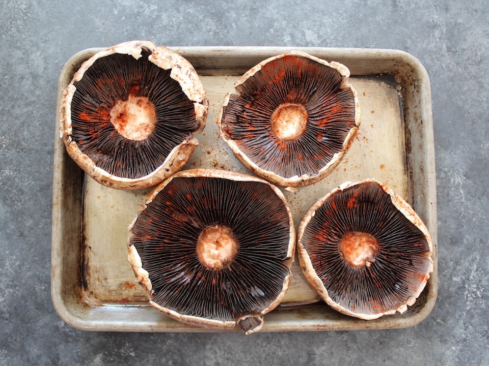 Portobello caps de-stemmed, four on a baking sheet, sprinkled with smoked paprika.