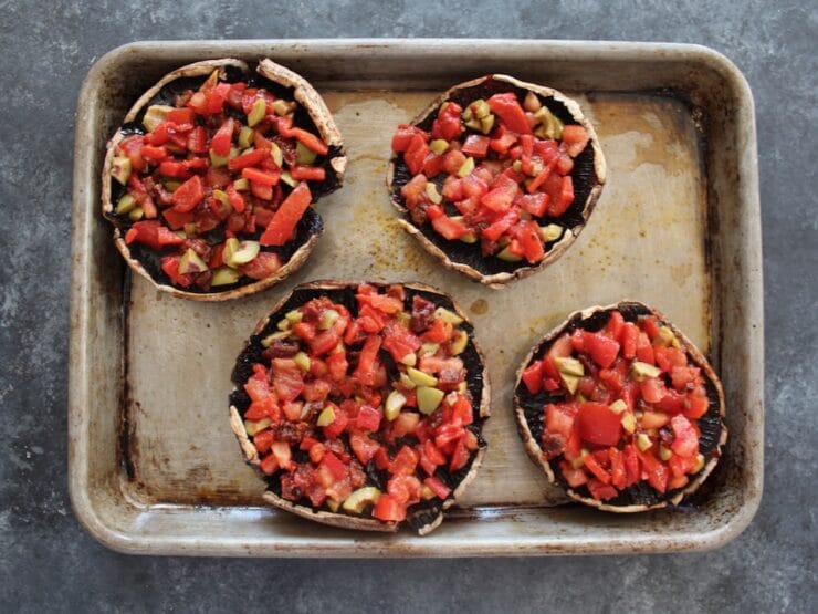 Vegetable-stuffed portobello caps, four on a baking sheet.