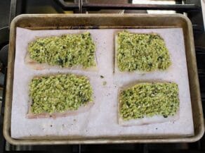 Sheet pan with four raw whitefish fillets topped with basil tapenade.