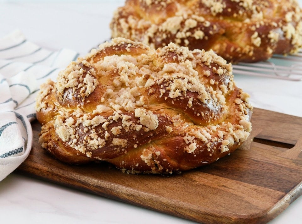 Horizontal shot of baked challah topped with a cinnamon crumble, sitting on a wooden cutting board.