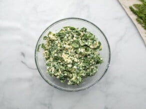 Horizontal overhead shot of a glass mixing bowl filled with a spinach, feta, and artichoke filling mixture.