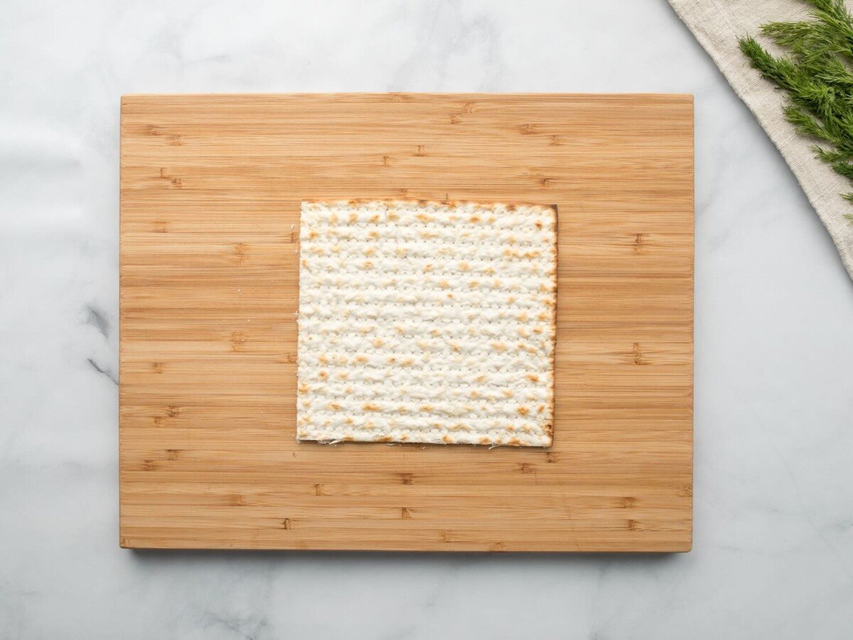 Horizontal overhead shot of a sheet of matzo laying on a wooden cutting board.
