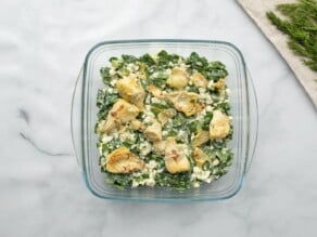 Horizontal overhead shot of a square glass baking dish filled with a spinach, feta, and artichoke filling mixture.