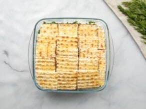 Horizontal overhead shot of a square glass baking dish filled with layered pieces of small matzo squares.