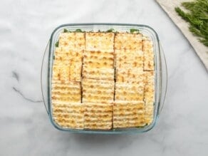 Horizontal overhead shot of a square glass baking dish filled with layered pieces of small matzo squares.
