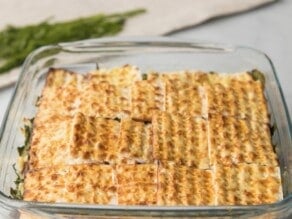 Horizontal shot of a square glass baking dish filled with layered pieces of small matzo squares.