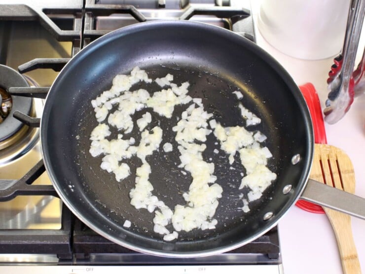 Overhead shot of diced white onion pieces sautéeing in a frying pan.