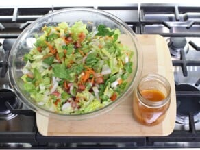 Overhead shot - salad ingredients in a bowl, with salad dressing in a small carafe alongside it, on a wooden cutting board.