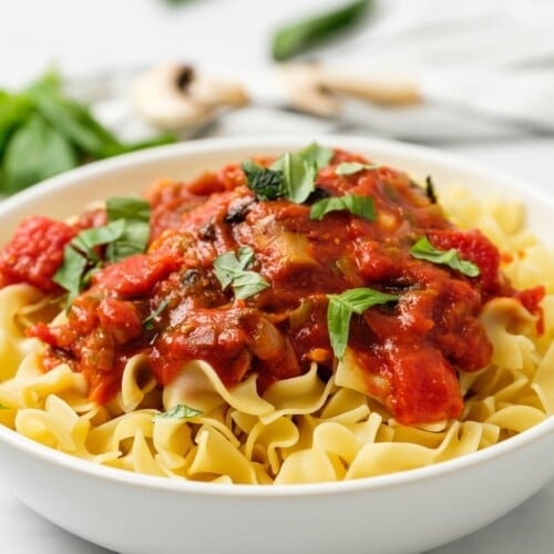 Horizonal shot of a bowl of egg noodles topped with chicken cacciatore in tomato sauce and garnished with parsley.