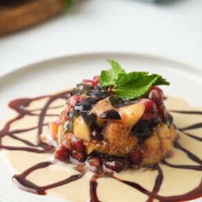 A beautiful Mediterranean dessert made with fresh fruit and drizzled sauce, topped with fresh mint, on a white plate.