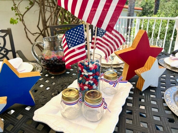 4th of July decorated table with candy centerpiece on platter, flags, wooden star decorations, small mason jars.