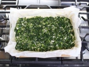 Horizontal overhead image of a glass baking dish containing slices of phyllo dough covered with a layer of vegan spanakopita filling.