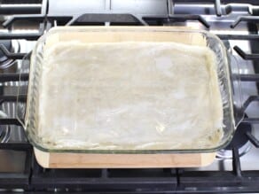 Horizontal overhead image of a glass baking dish containing un-cooked spanakopita sitting on the stove top.