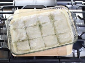 Horizontal overhead image of a glass baking dish containing un-cooked spanakopita sitting on the stove top.