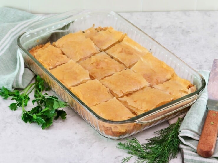 Horizontal image of a glass baking dish containing vegan spanakopita that has been cut into squares.