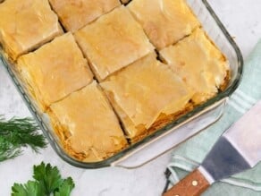 Horizontal overhead image of a glass baking dish containing vegan spanakopita that has been cut into squares.