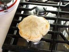 Pita baking and puffing up on top of a gas stovetop burner.