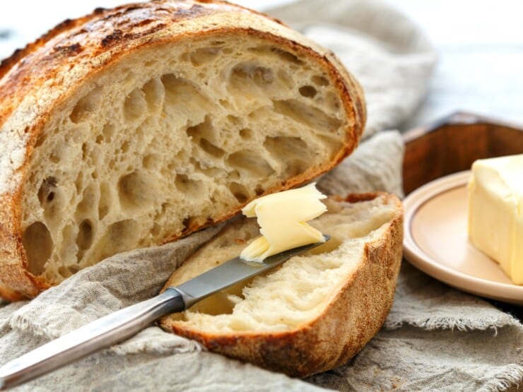 Sliced boule of sourdough, knife with butter, small plate with butter on the side.