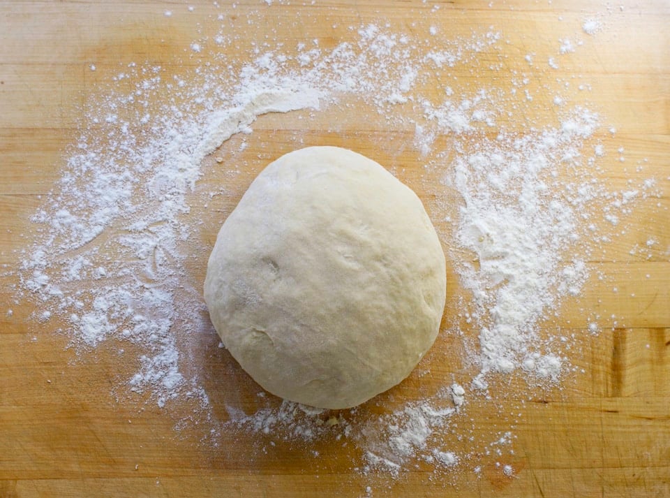 A ball of smooth dough rests on a floured wooden surface.