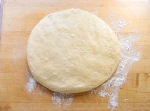 Round, smooth and slightly risen dough on a wooden surface, dusted with flour.