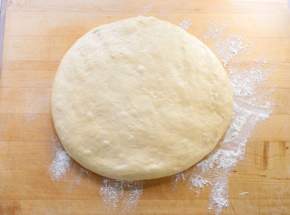 Round, smooth and slightly risen dough on a wooden surface, dusted with flour.