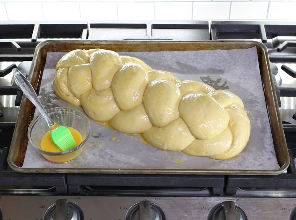 A baking sheet holds a braided bread, with a bowl of butter and brush nearby.