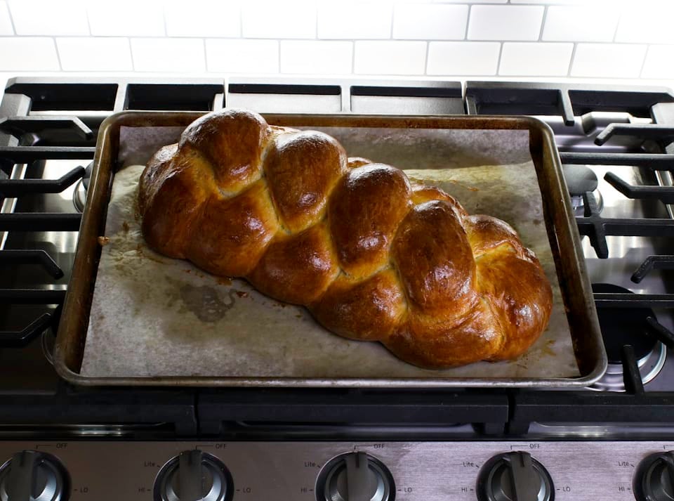 A dark golden-brown braided challah bread placed on a baking sheet, emphasizing its beautiful shape and crusty exterior.