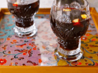 The Smoking Bishop Pin - Two ornate glasses filled with Smoking Bishop sit on a colorful floral tray. A large pitcher in the background adds a festive feel to the scene.